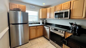 A compact kitchen with wooden cabinets, a stainless steel refrigerator, a microwave, an oven, and a black countertop. - 2 minutes to the beach (Pensacola Beach)