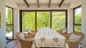 A dining area with a table and wicker chairs, large windows, and a view of greenery. - 'Villa Casa Colina'with Pool and Wi-Fi (Albir)
