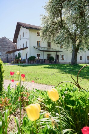 Un bâtiment à deux étages, doté d’un toit en pente, d’un patio couvert et d’une pelouse bien entretenue agrémentée de fleurs.