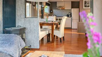 A modern kitchen with a dining area, wooden flooring, and a large window.