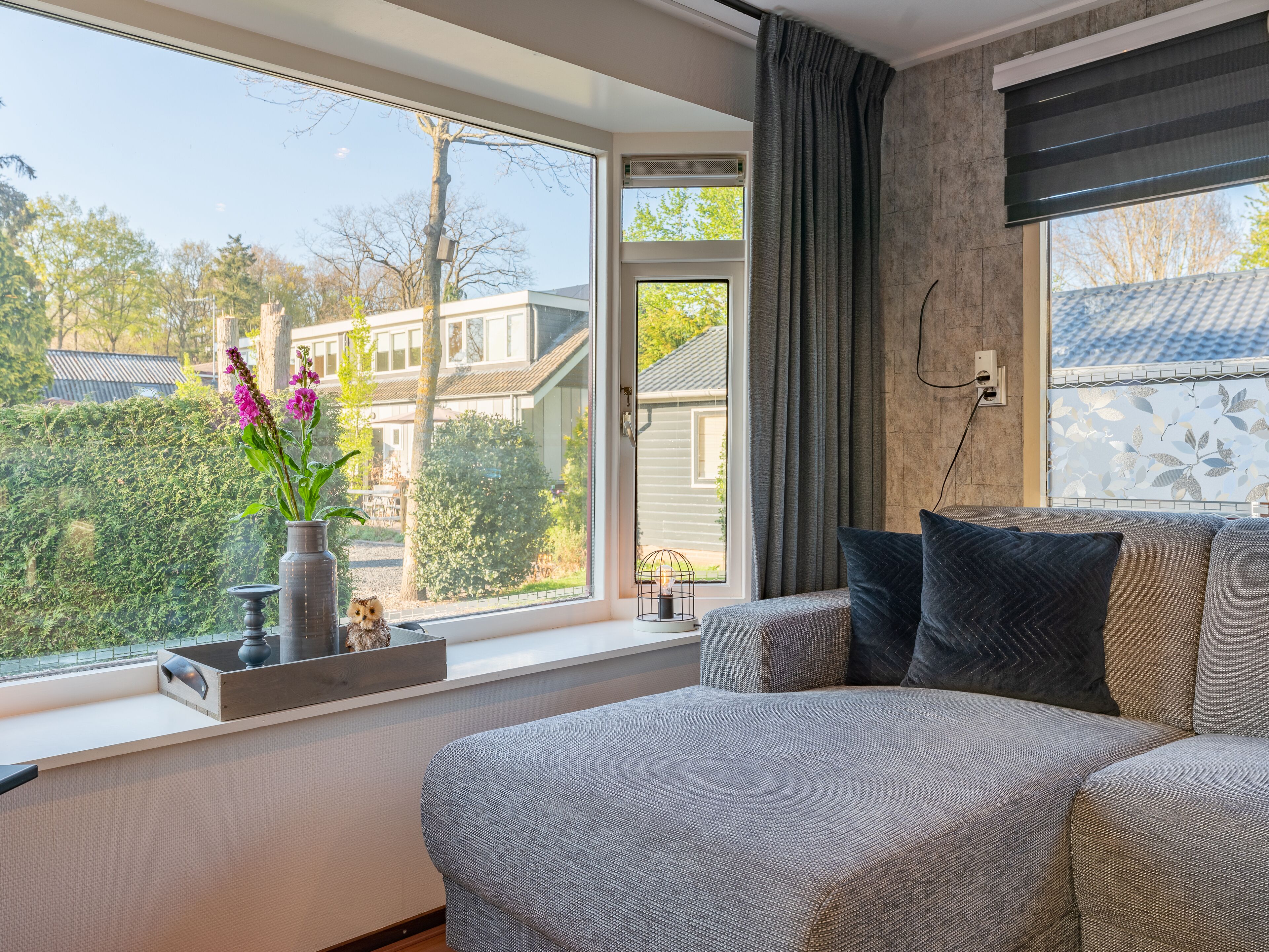 Een moderne slaapkamer met een groot raam, een grijze bank en een vaas met bloemen.