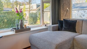 A modern bedroom with a large window, a grey sofa, and a vase with flowers. - Romantic chalet on the Veluwe (Hulshorst)