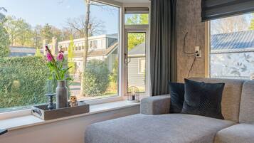 Een moderne slaapkamer met een groot raam, een grijze bank en een vaas met bloemen.