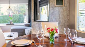 A dining table set with plates, cutlery, and wine glasses, a vase with flowers, and a 'Welcome' sign on the wall.