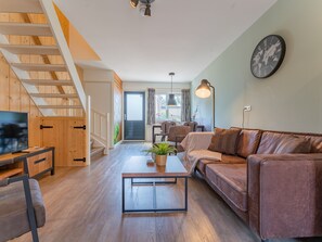 A modern living room with a wooden staircase, a sofa, a coffee table, and a television.