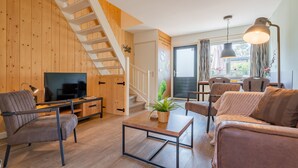 A modern living room with a wooden staircase, a flat-screen TV, a coffee table, and comfortable seating. - Modern tiny house for families on the Veluwe (Hulshorst)