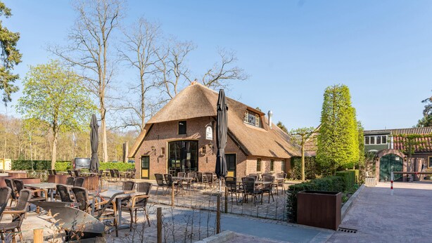 A rustic building with a thatched roof, outdoor seating area with wicker chairs, and a paved walkway. - Modern tiny house for families on the Veluwe (Hulshorst)