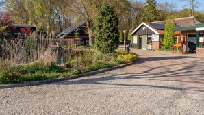 A building with a gravel driveway, a pond, and surrounding trees. - Modern tiny house for families on the Veluwe (Hulshorst)
