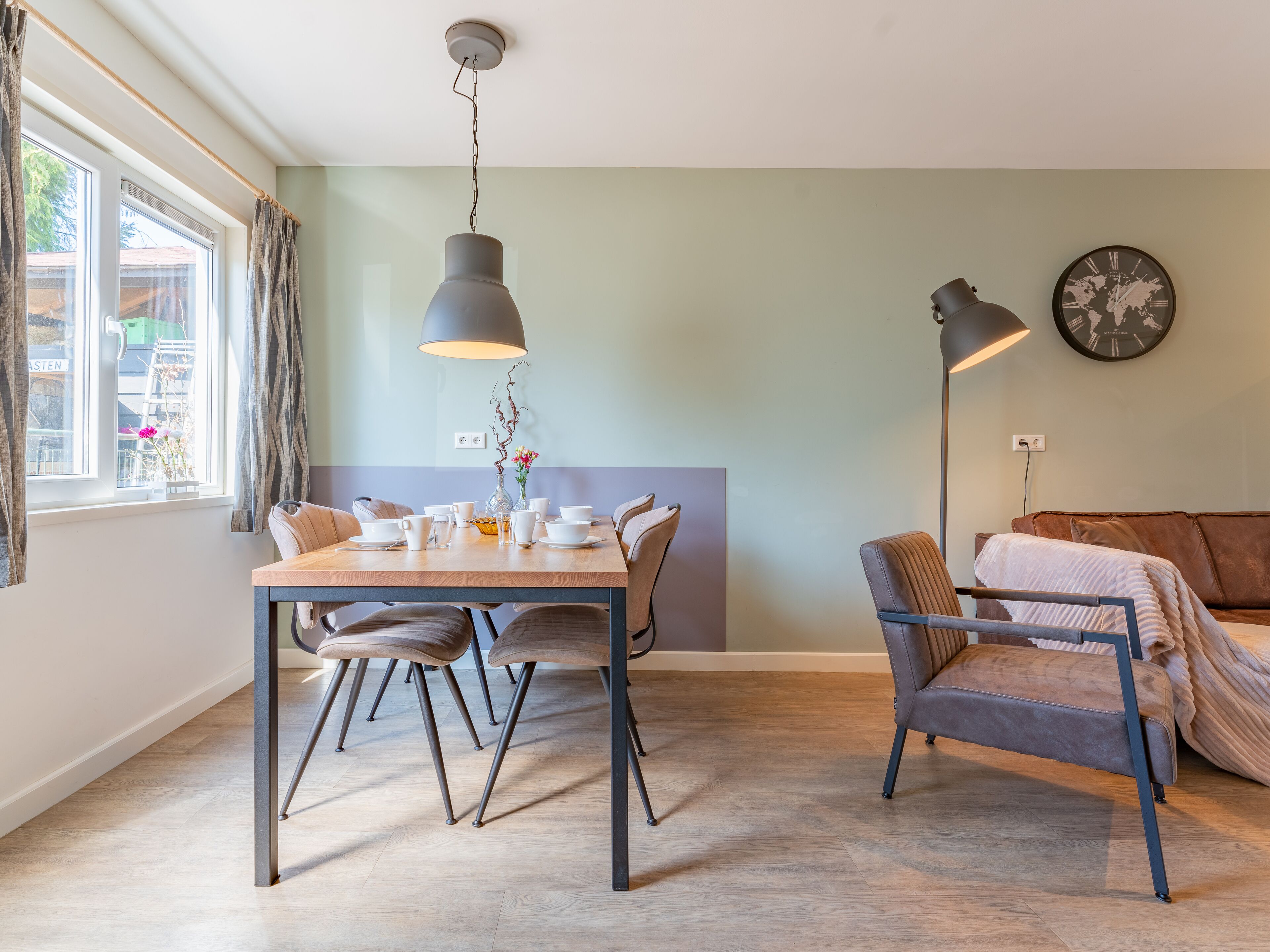 Un comedor con una mesa dispuesta para cuatro personas, un sofá y un reloj en la pared.