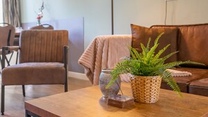 A cozy living room with a wooden coffee table, a woven basket with a fern, and a glass vase with a plant. - Modern tiny house for families on the Veluwe (Hulshorst)