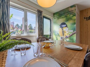 Enjoy meals with a view of the outdoors from this dining area, featuring a large window and a wall-mounted TV showcasing a serene landscape.