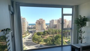 Une pièce spacieuse dotée d’une grande porte-fenêtre coulissante donnant sur un balcon, d’où l’on peut admirer un panorama sur la ville et les palmiers.