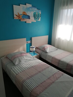 Une chambre avec deux lits, une table de chevet avec une lampe et un mur orné de trois tableaux.