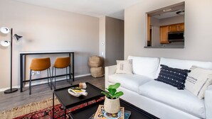 A modern living room with a white sofa, two orange chairs, a coffee table with a plant, and a magazine. A dining area with a table and chairs is visible in the background. - Rockin on the River!!! (Nashville)