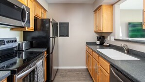 A compact kitchen with wooden cabinets, a black countertop, a stainless steel refrigerator, a microwave, and a stove. - Rockin on the River!!! (Nashville)