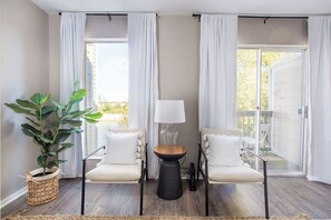 Una habitación con dos sillas blancas, una mesita y una planta en maceta.
