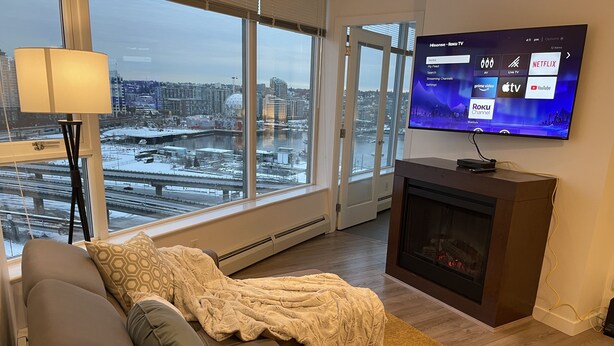 Een moderne woonkamer met een groot raam, een open haard en een televisie waarop de Roku TV interface te zien is.
