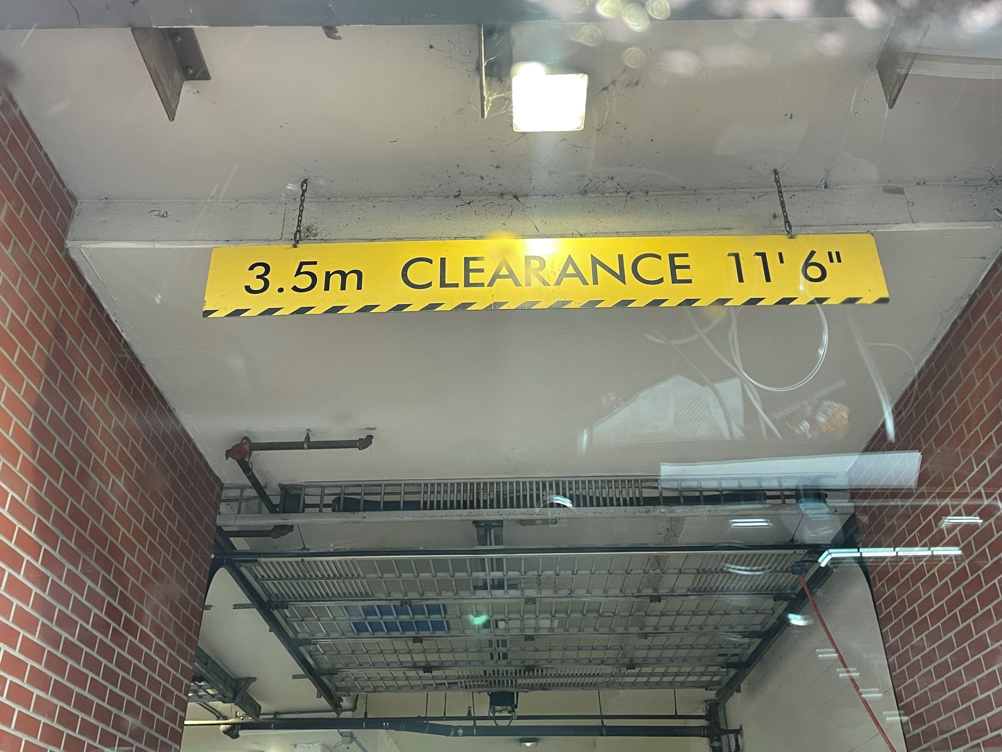 Un aparcamiento con un cartel amarillo que indica una altura máxima de 3,5 metros y 11 pies y 6 pulgadas.