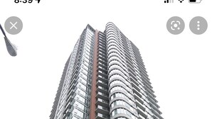 Een hoog, modern hoogbouwgebouw met een gebogen gevel en meerdere balkons, met een rode auto ervoor geparkeerd.
