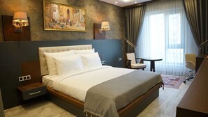 Una camera d'albergo con un letto grande, una scrivania, una sedia e un quadro appeso al muro.