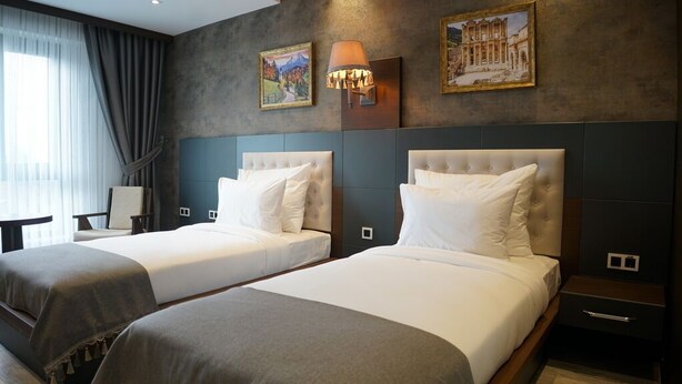 Camera d'albergo con due letti, un comodino, una lampada e opere d'arte alle pareti.