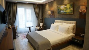 Camera d'albergo con un letto grande, una scrivania, una sedia e un tavolino. Due lampade a parete e un quadro sopra il letto.