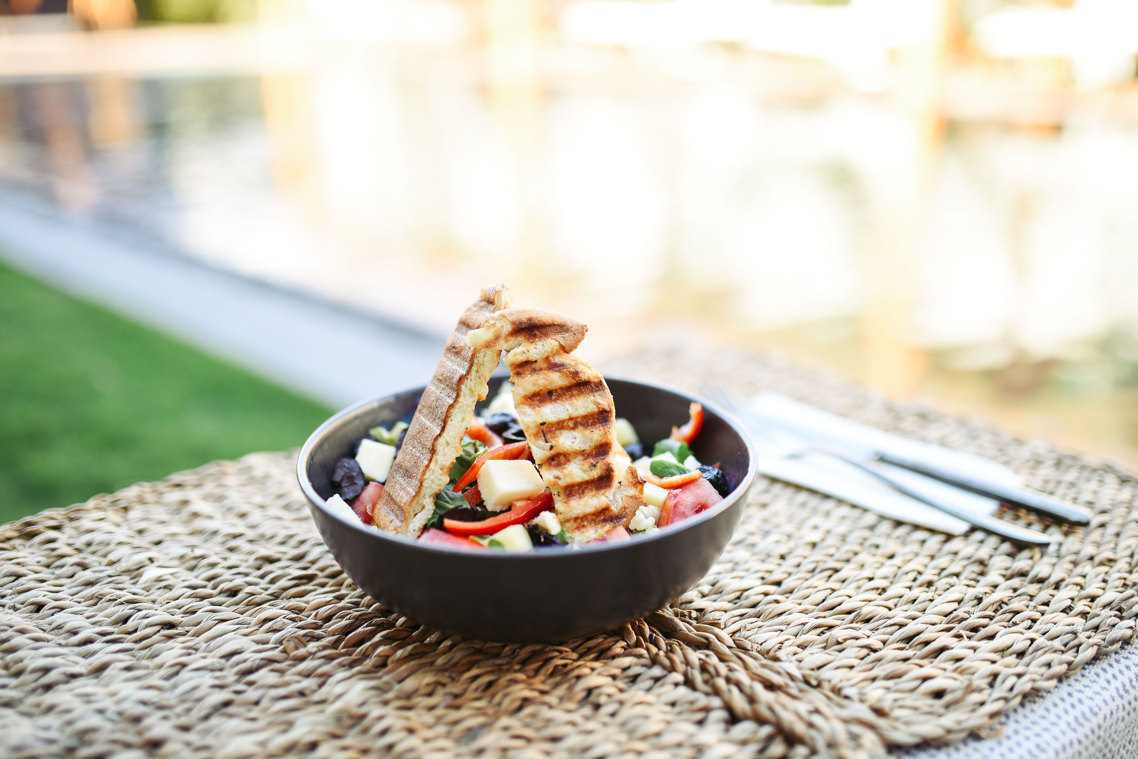 A bowl of salad with grilled bread on a woven mat.