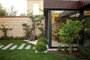 Una casa moderna con un muro de piedra, un césped cuidado y un área de comedor visible a través de puertas de vidrio.