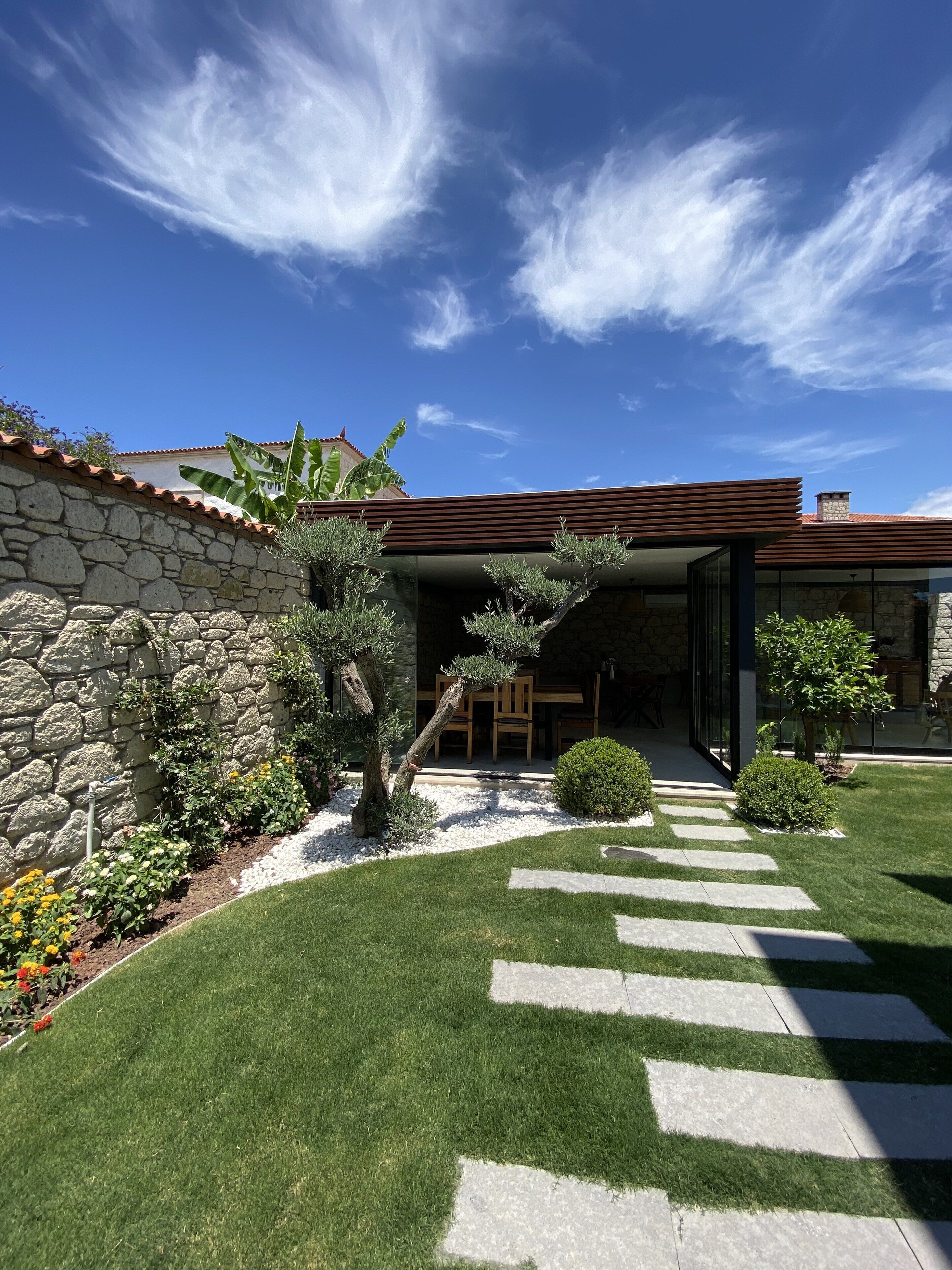 A modern house with a stone wall, a well-maintained lawn, and a clear sky.