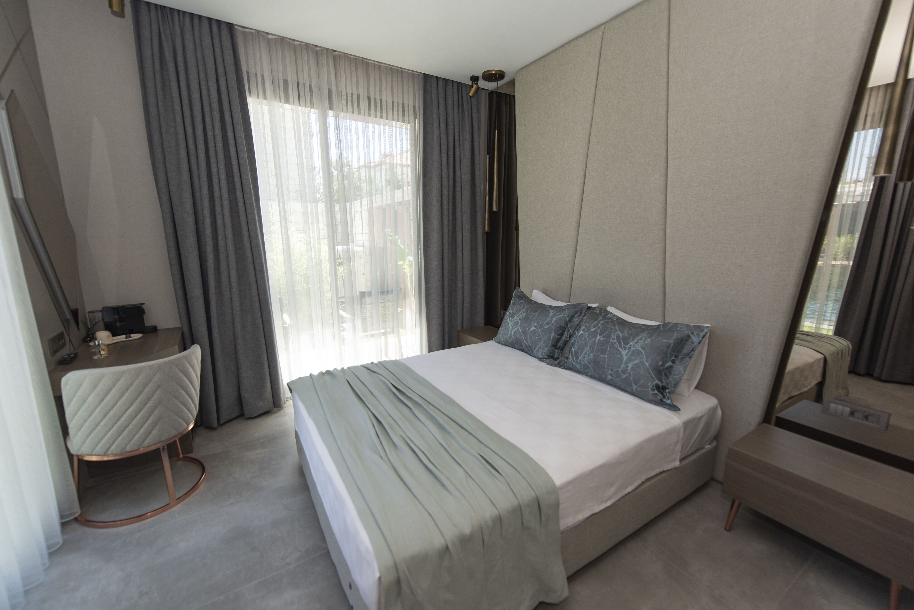 Habitació d'hotel moderna amb un llit gran, una taula de nit, un escriptori i una finestra amb cortines.