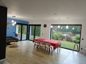 Un comedor moderno con una mesa roja, sillas blancas y vistas a un jardín a través de ventanas amplias.