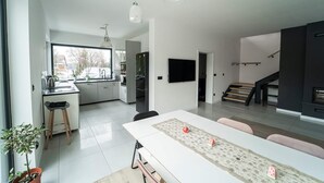 A modern kitchen with a dining area, a TV mounted on the wall, and a staircase leading to an upper level.