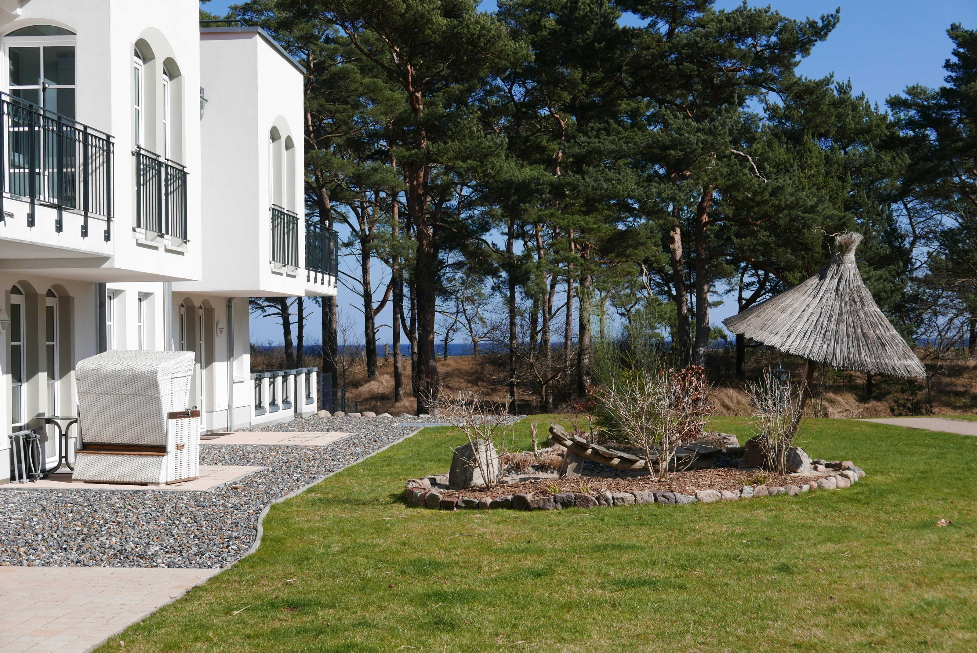 Een wit gebouw met een balkon, een rieten stoel en een rieten constructie in de tuin.