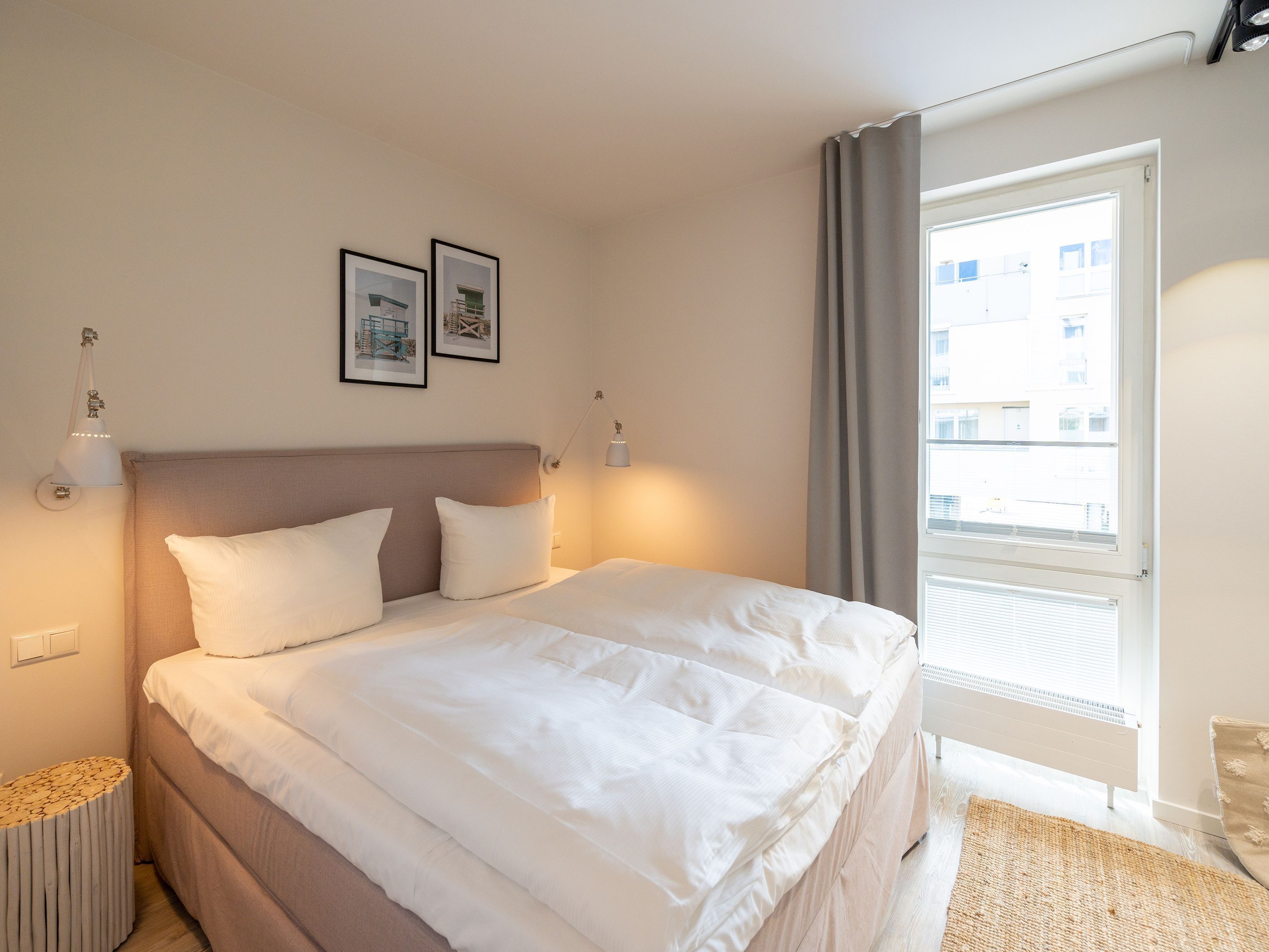 Una cama bien hecha con ropa de cama blanca, un cabecero y dos cuadros en la pared.