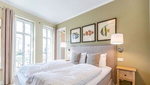 Een slaapkamer met een groot bed, een nachtkastje, een lamp en drie ingelijste foto's aan de muur.