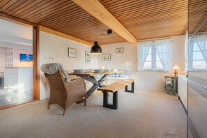 Un coin repas avec un plafond en bois, une chaise en osier, un banc, une table avec des bols et une lampe.