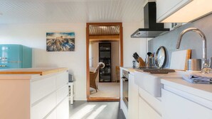 A modern kitchen with white cabinetry, a blue refrigerator, and a wooden dining area visible through an open doorway.