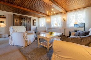 Un salon chaleureux avec un plafond en bois, un canapé blanc, un canapé beige, une table à manger avec un saladier et un tableau accroché au mur.