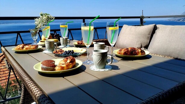 Ein Tisch, reichhaltig mit Frühstücksleckereien und Getränken gedeckt, mit Blick auf eine malerische Meereslandschaft.
