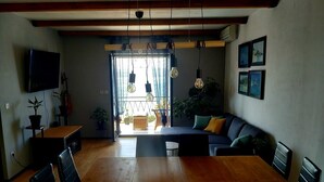 Ein Esszimmer mit Holztisch und -stühlen, einer Couch und einem an der Wand befestigten Fernseher.