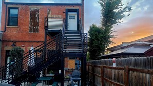 A brick building with a metal staircase leading to a door, outdoor seating, and a wooden fence with a reserved parking sign. - Luxurious, downtown loft with a warm, family feel (Sheridan)