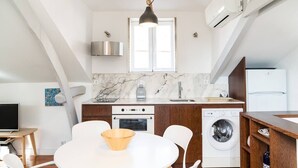 Een moderne keuken met een marmeren aanrecht, een ingebouwde oven, een wasmachine en een eethoek met een ronde tafel en stoelen.
