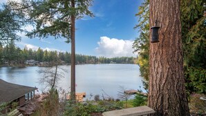 A serene lakeside view with a large tree, a stone bench, and a bird feeder. - Koi Story Cabin - Lakefront, near Bike Trail (Maple Valley)