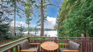 A wooden deck with a round table and four wicker chairs, overlooking a lake with trees and a clear sky. - Koi Story Cabin - Lakefront, near Bike Trail (Maple Valley)