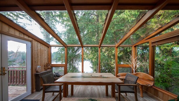 A wooden cabin with a large dining table and chairs, surrounded by large windows offering views of a forest and a lake. - Koi Story Cabin - Lakefront, near Bike Trail (Maple Valley)