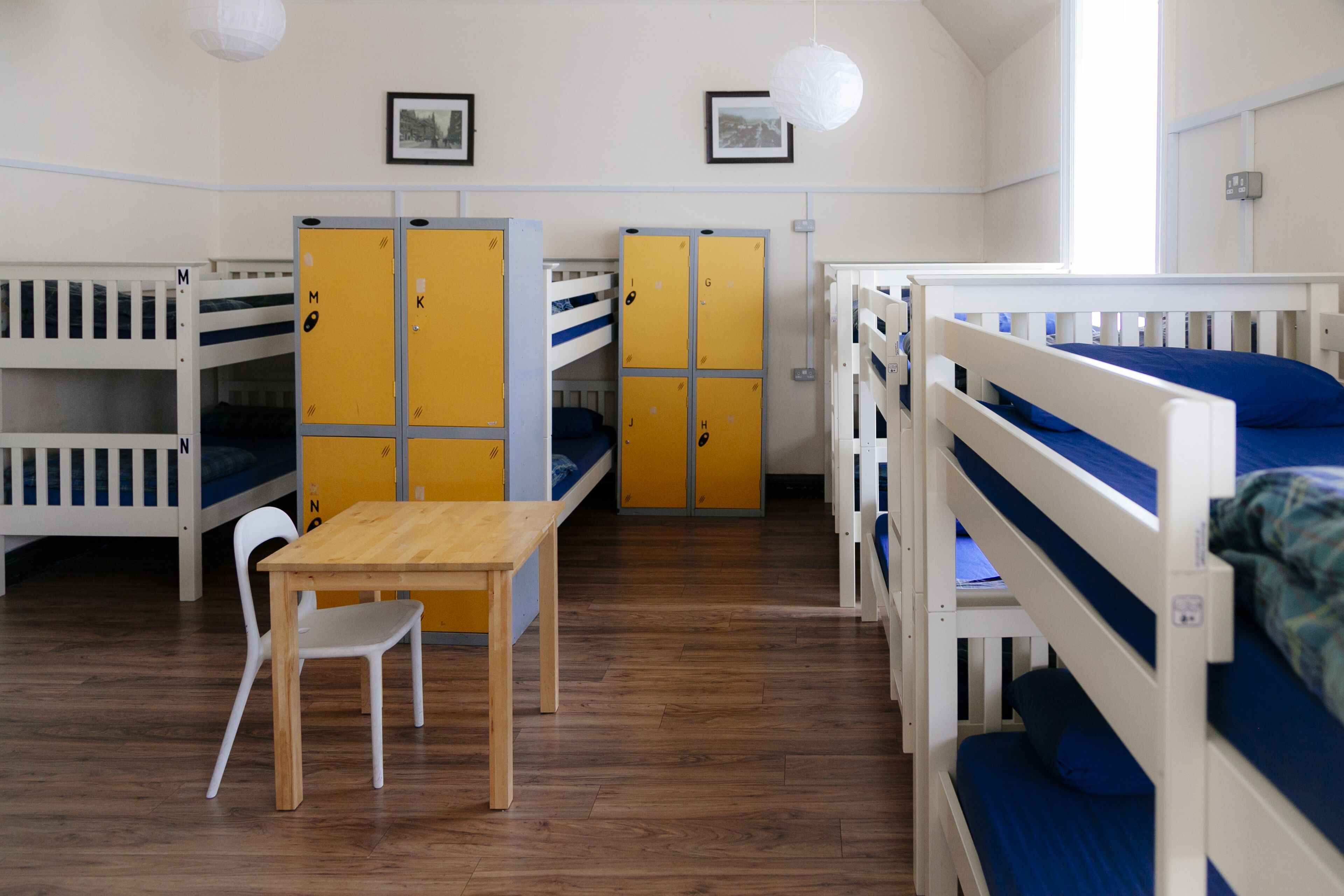 A dormitory room with bunk beds, a wooden table, and chairs.