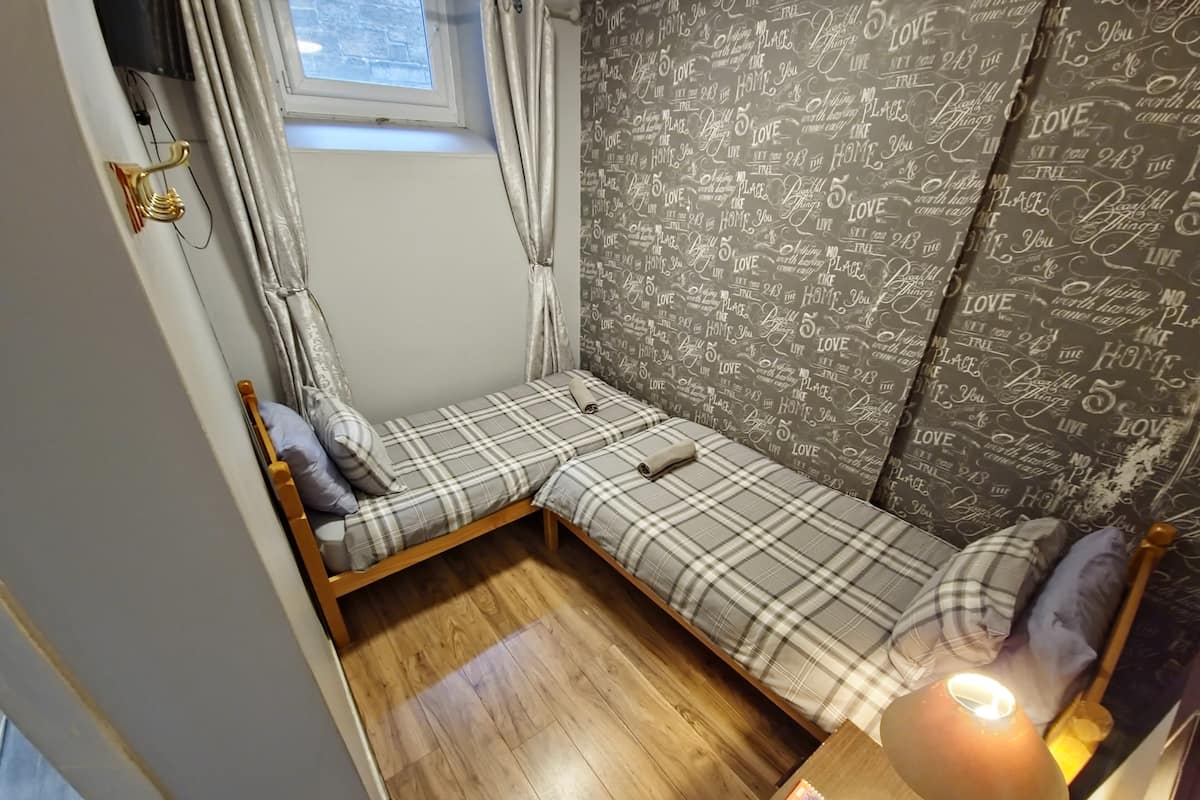 Ein kleines, gemütliches Zimmer mit einem Einzelbett, einem Nachttisch mit Lampe und einem Fenster mit Vorhängen.