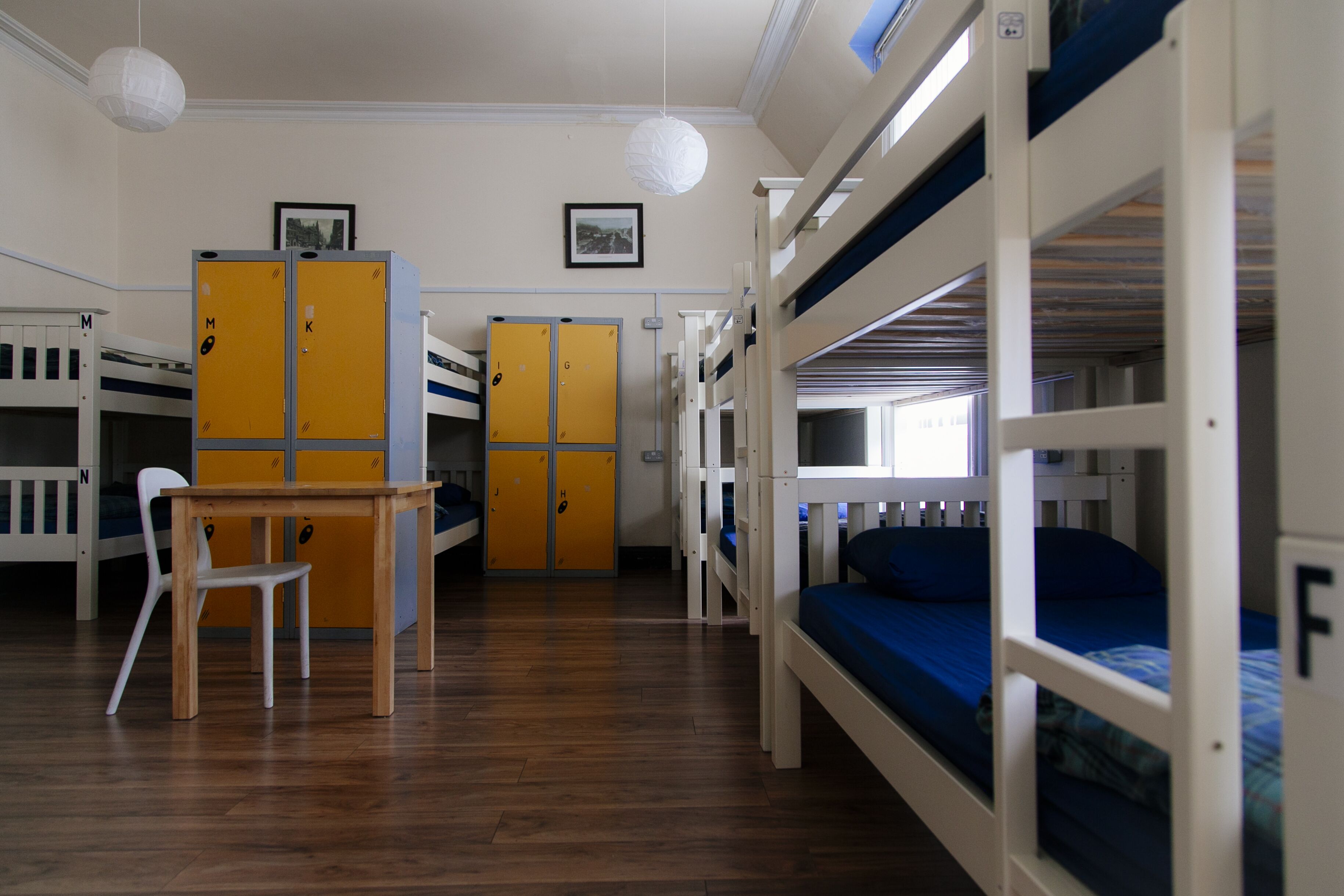 Une chambre de dortoir avec des lits superposés, un bureau en bois, une chaise et des casiers.