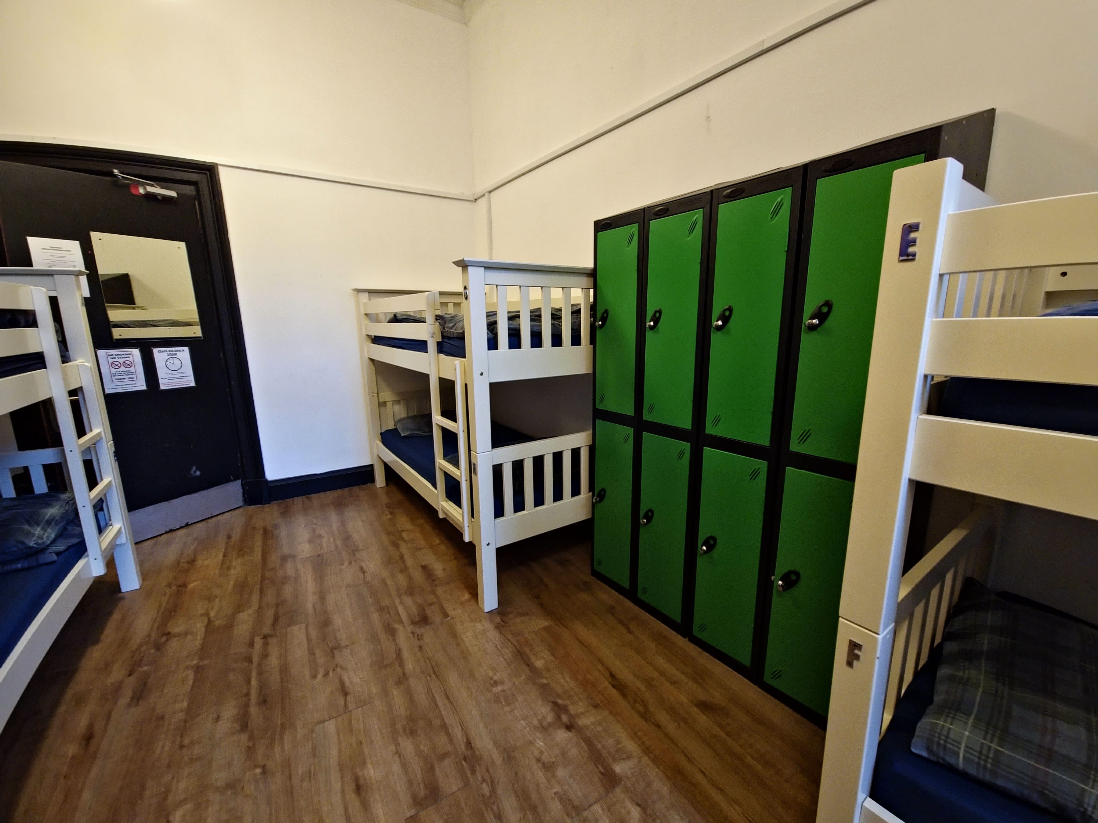 Ein Schlafsaalzimmer mit Etagenbetten, einer Tür mit einem Schild und grünen Schließfächern.