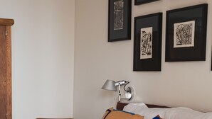 Et hotelværelse med en seng, en stol, en lampe og indrammet kunst på væggen.